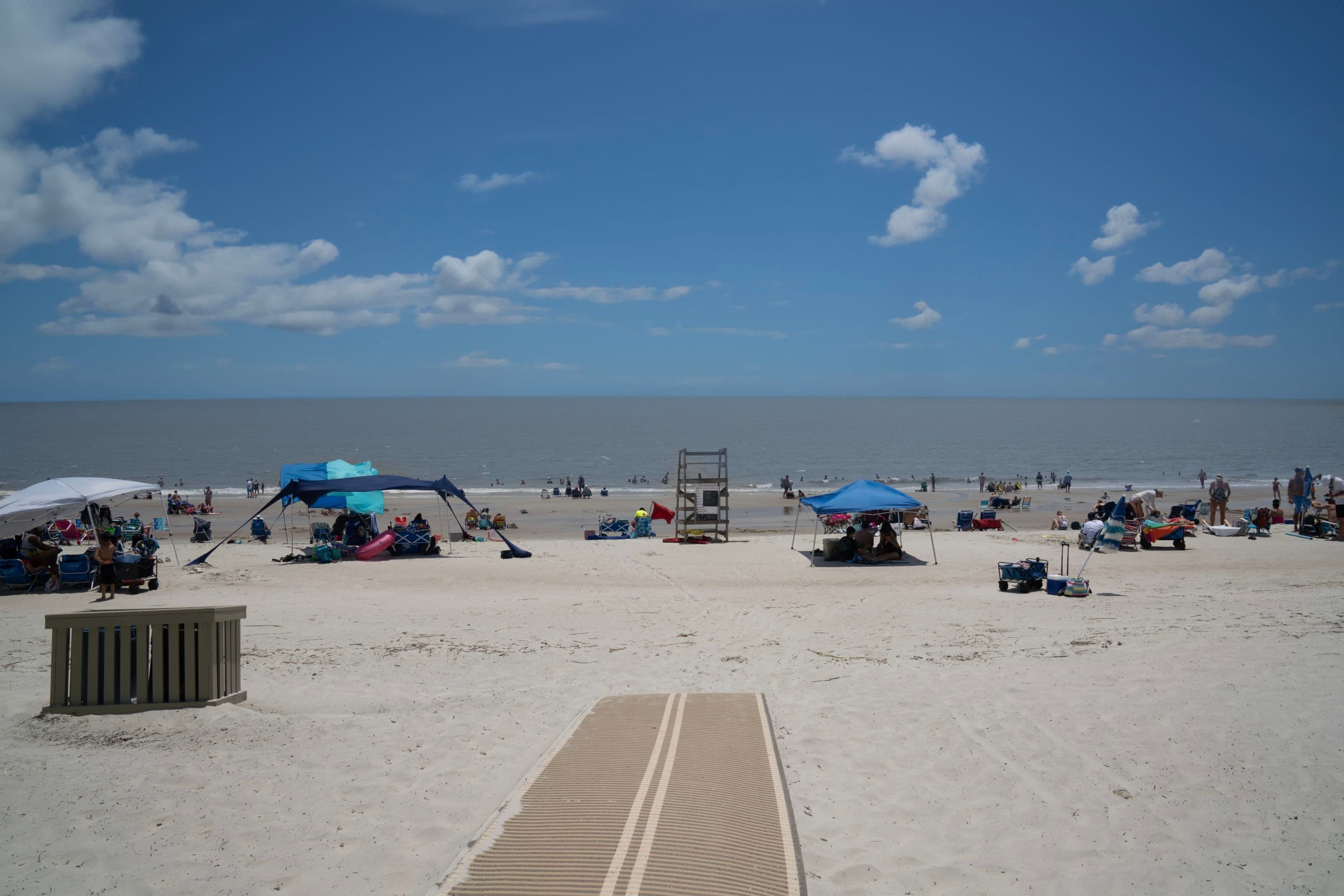 A beach with a sandy walkway leading to the water, beach chairs, umbrellas, and a lifeguard tower.
