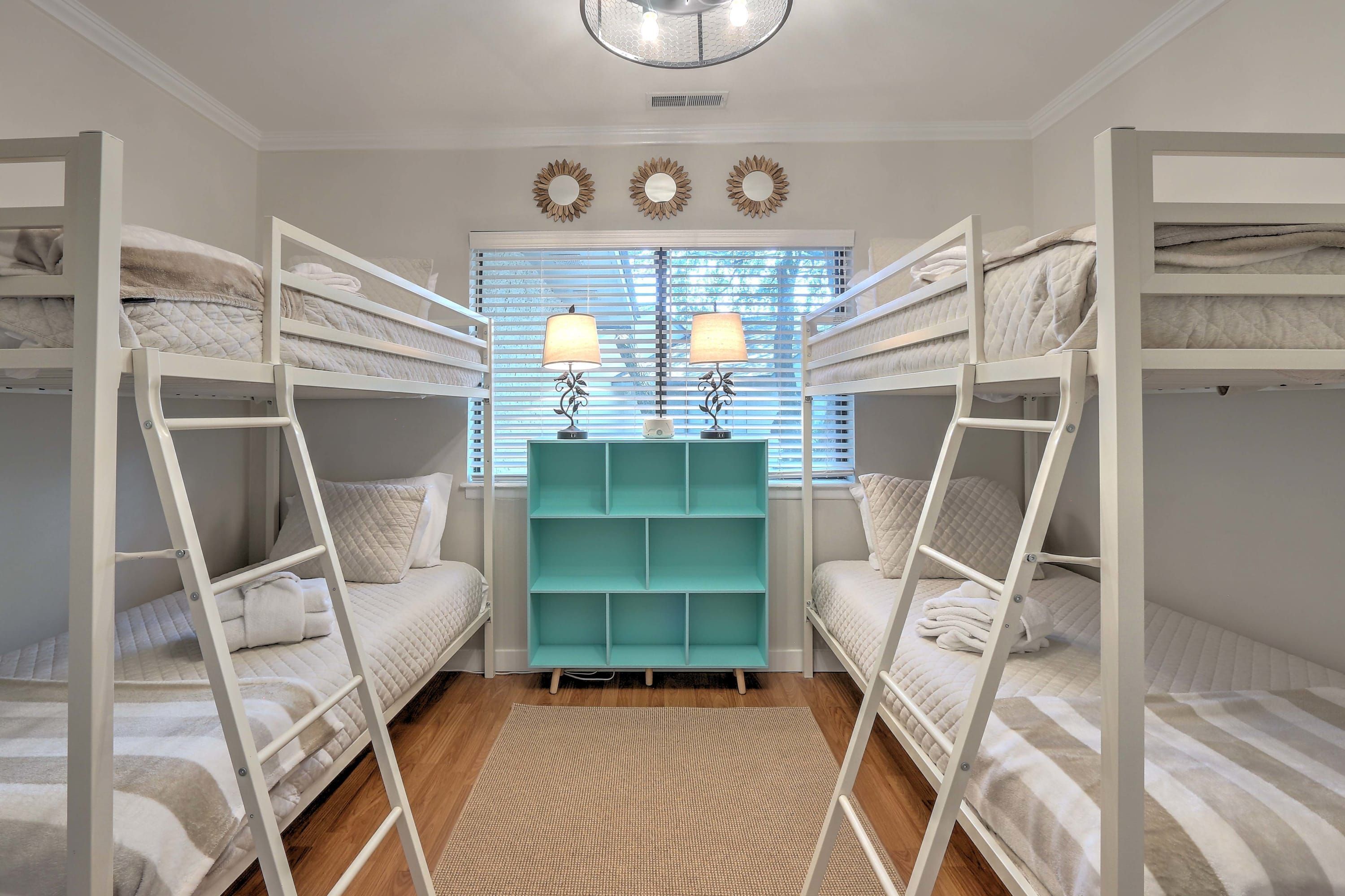 Une chambre avec un lit superposé, un meuble de rangement turquoise et deux lampes fixées au mur.