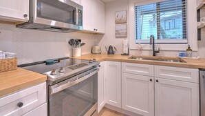 Una cocina moderna con armarios blancos, electrodomésticos de acero inoxidable, horno integrado y ventana con persianas.