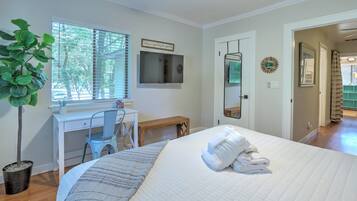 Un dormitorio con cama, escritorio, silla, televisor y una planta.