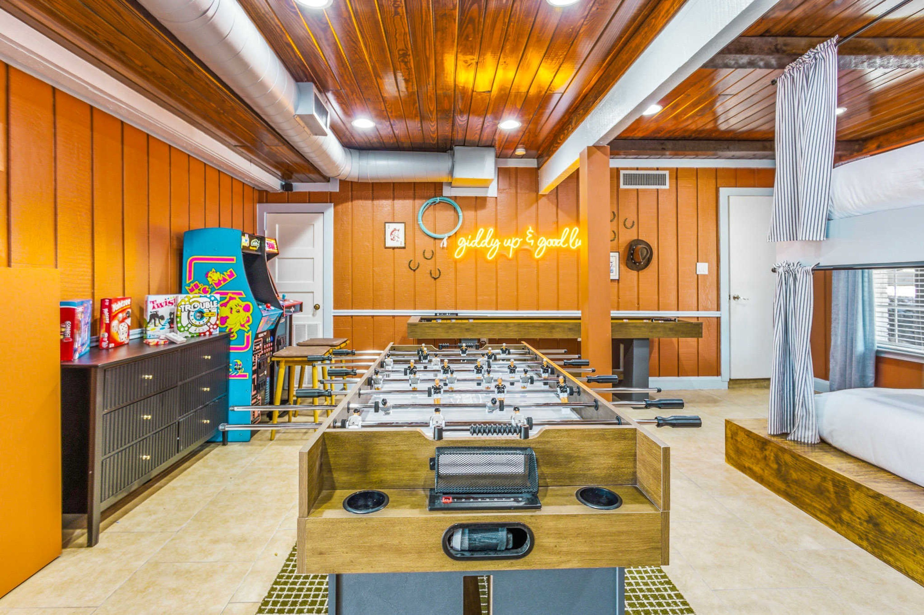 Una habitación con mesa de fútbol, letrero de neón y una cama con cortinas a rayas.