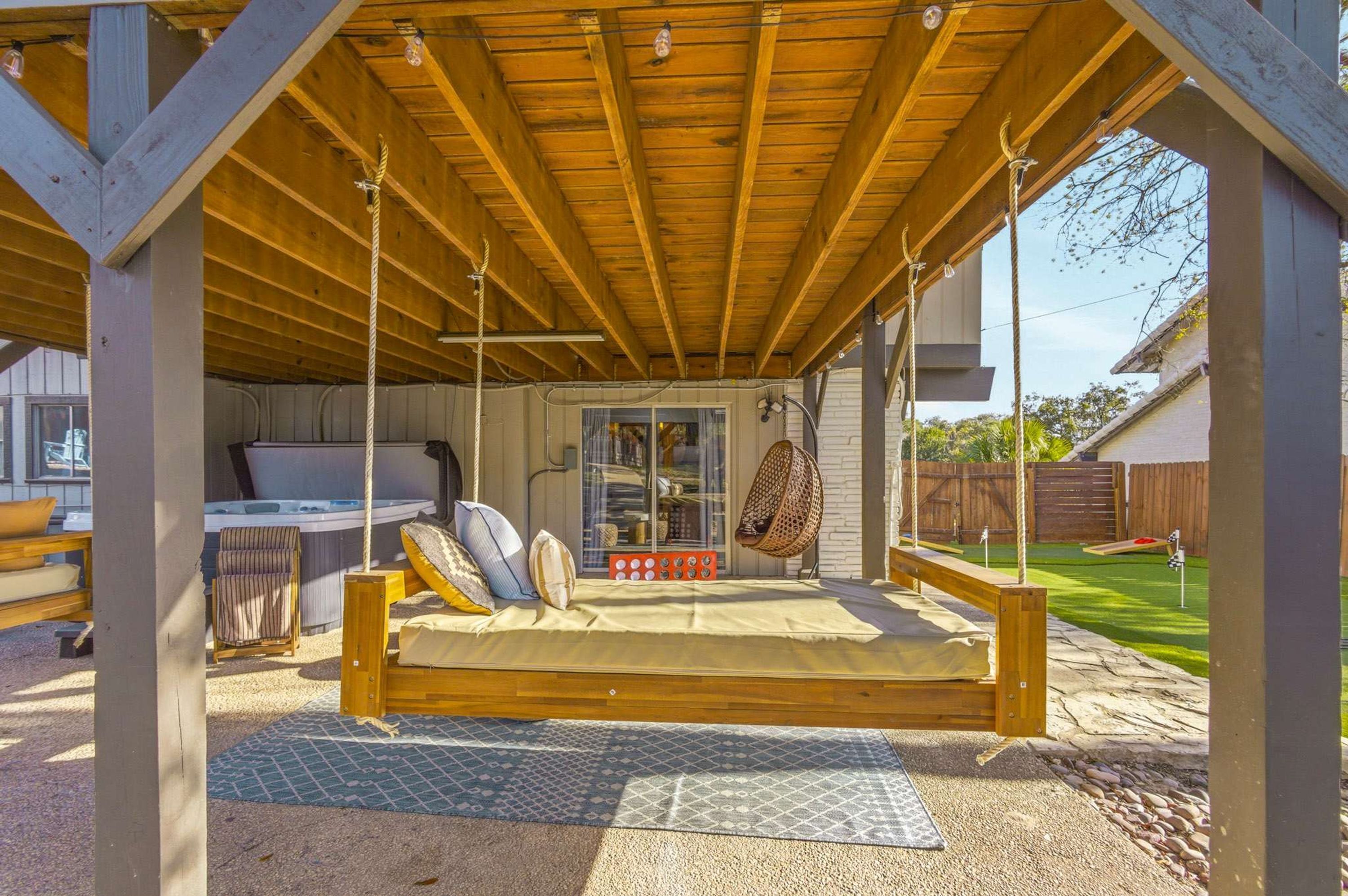 A wooden swing set with a cushioned seat and backrest, a hot tub, and a wicker chair in a covered outdoor area.