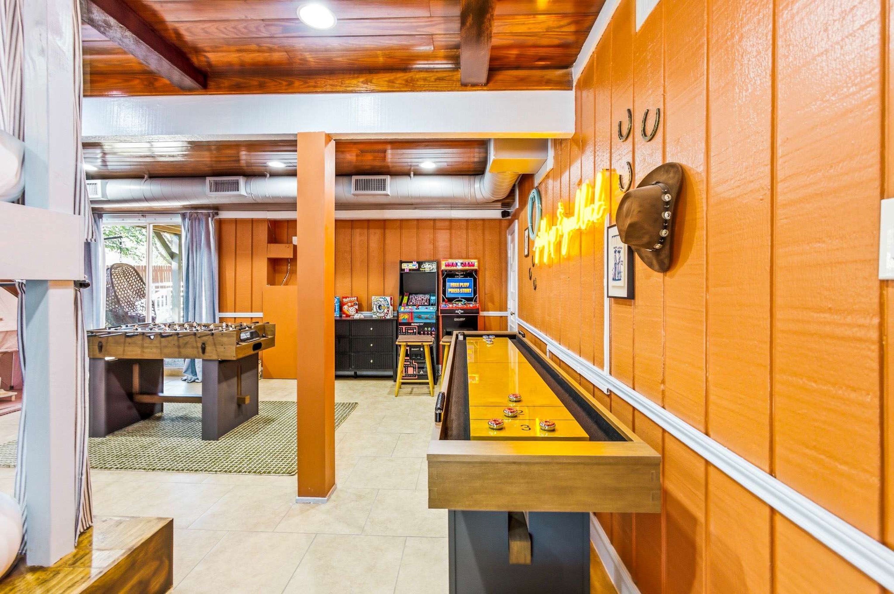A room with a foosball table, a shuffleboard table, and arcade games.