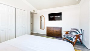 Een slaapkamer met een bed, een kaptafel, een stoel en een aan de muur bevestigde televisie.
