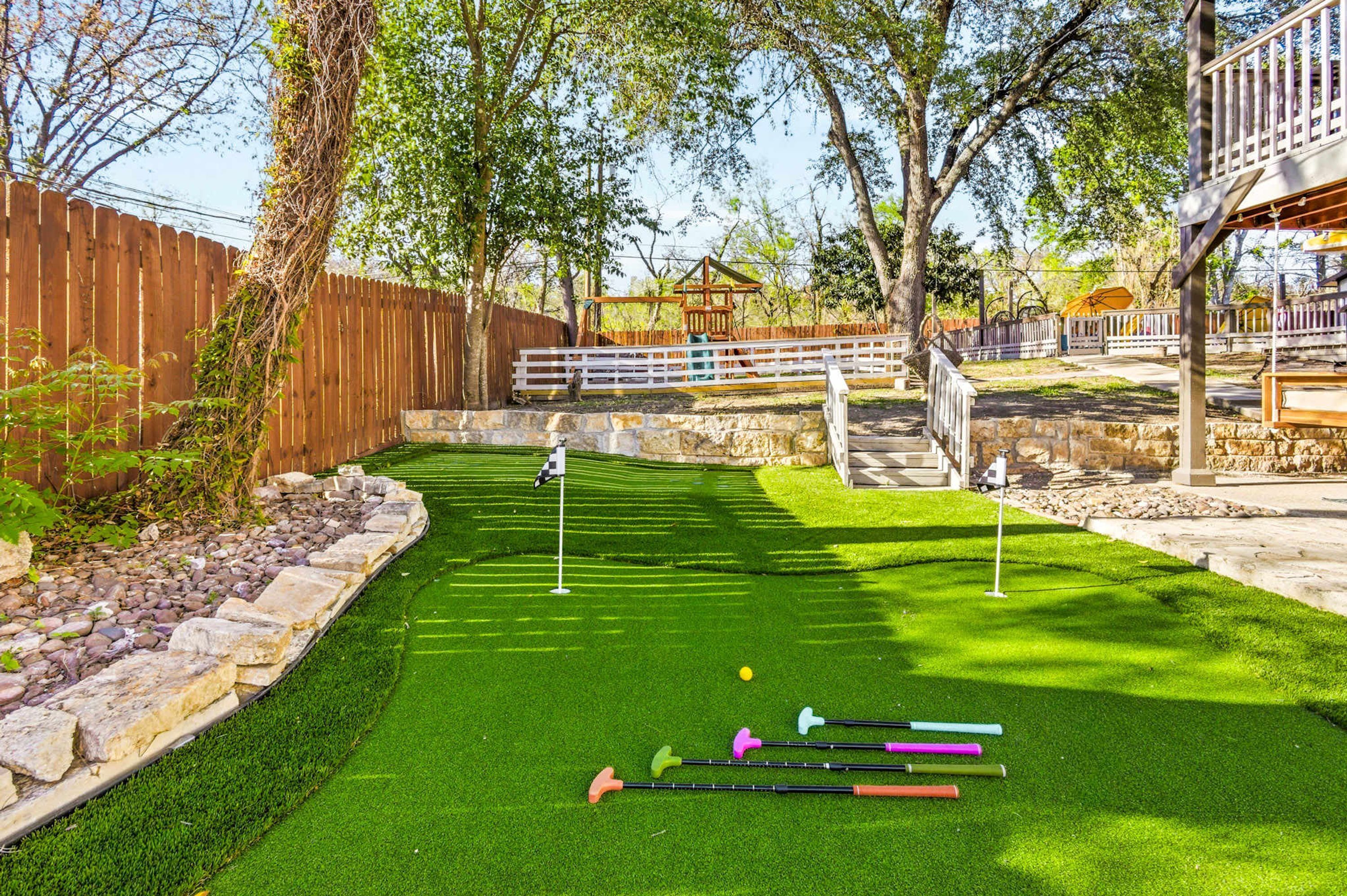 A well-maintained backyard with a putting green, a wooden fence, and a stone wall.