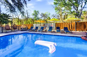 A swimming pool with lounge chairs and umbrellas, surrounded by a wooden fence and trees. - Private Resort 4 Baths Near Pearl (San Antonio)