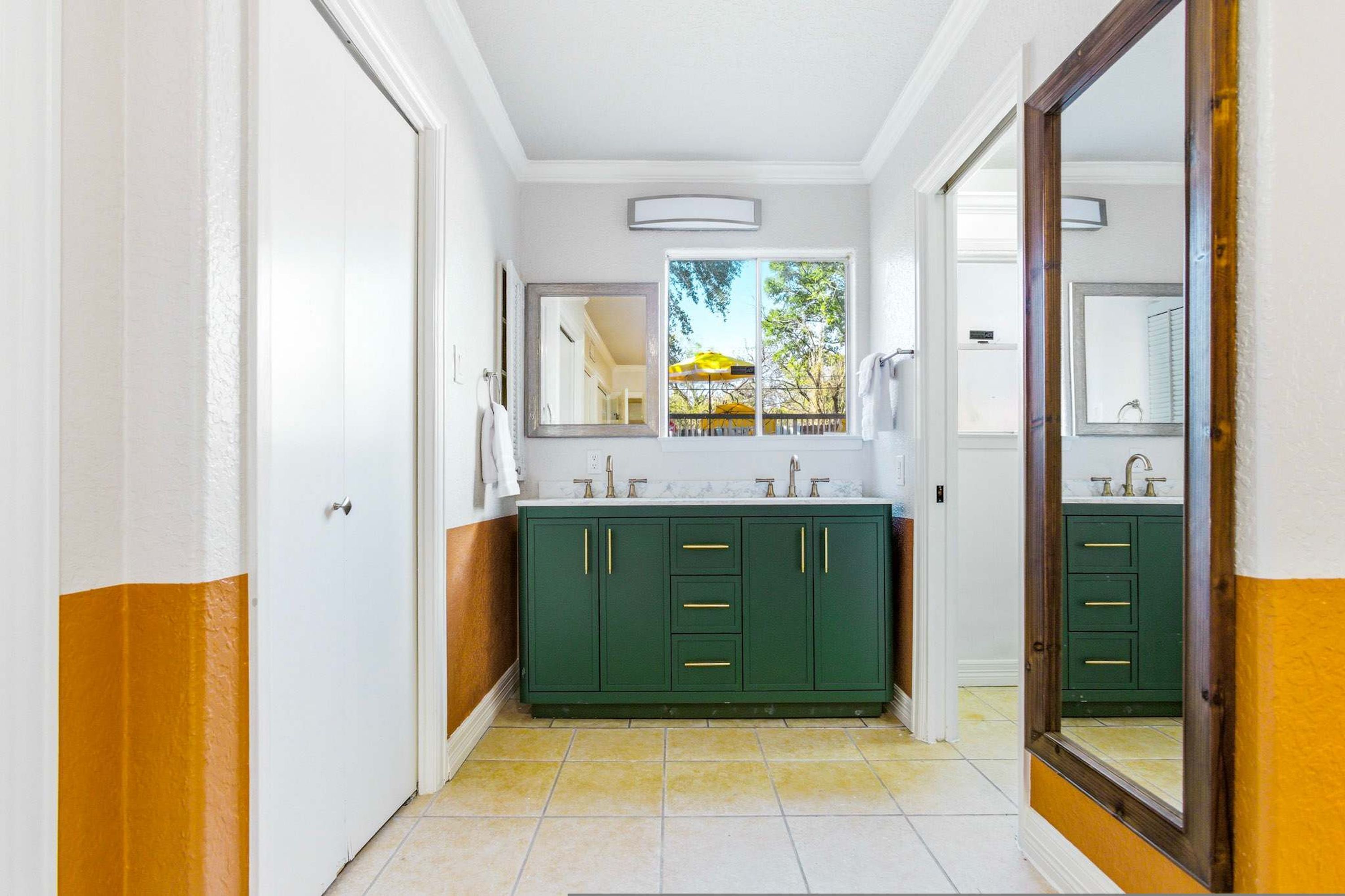 A bathroom with a double sink, green cabinets, and a large mirror.