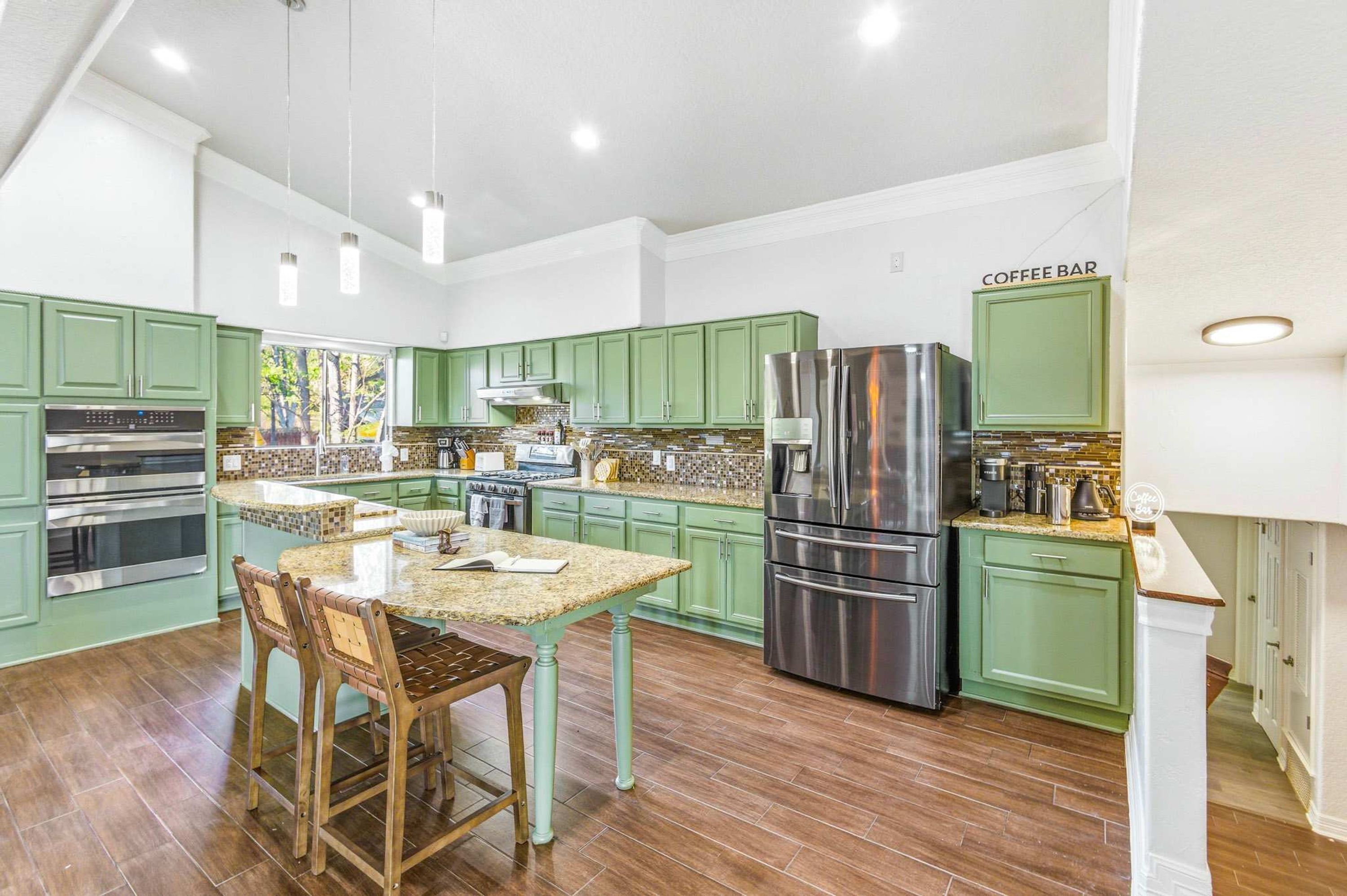 A modern kitchen with green cabinets, stainless steel appliances, and a coffee bar.