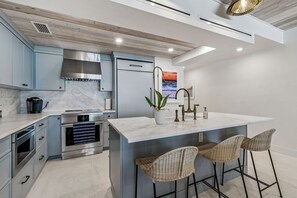 Une cuisine moderne dotée d’un îlot central, de tabourets de bar et offrant une vue sur l’océan par une fenêtre.