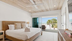 A bedroom with a wooden bed, a ceiling fan, a view of the sea, and a balcony with a chair. - Beachfront Bliss - Outdoor Pool - Sleeps 6 (Belleair Beach)