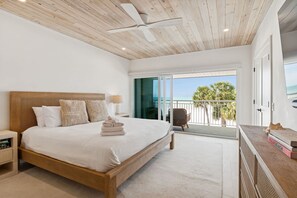A bedroom with a wooden bed, a ceiling fan, a view of the sea, and a balcony with a chair. - Beachfront Bliss - Outdoor Pool - Sleeps 6 (Belleair Beach)
