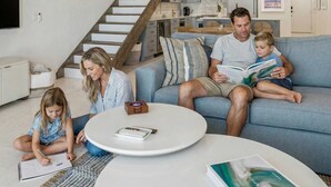 A modern living room with a blue sofa, a round coffee table, and a staircase with wooden steps. - Beachfront Bliss - Outdoor Pool - Sleeps 6 (Belleair Beach)