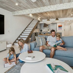 A modern living room with a blue sofa, a round coffee table, and a staircase with wooden steps. - Beachfront Bliss - Outdoor Pool - Sleeps 6 (Belleair Beach)