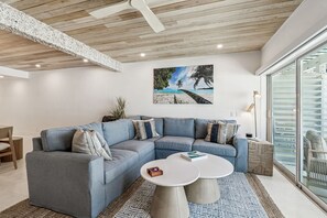 A modern living room with a sectional sofa, two coffee tables, and a beach-themed painting on the wall. - Beachfront Bliss - Outdoor Pool - Sleeps 6 (Belleair Beach)