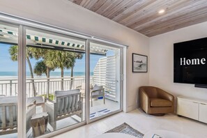 A modern living room with a large sliding glass door leading to a balcony overlooking a beach. - Beachfront Bliss - Outdoor Pool - Sleeps 6 (Belleair Beach)