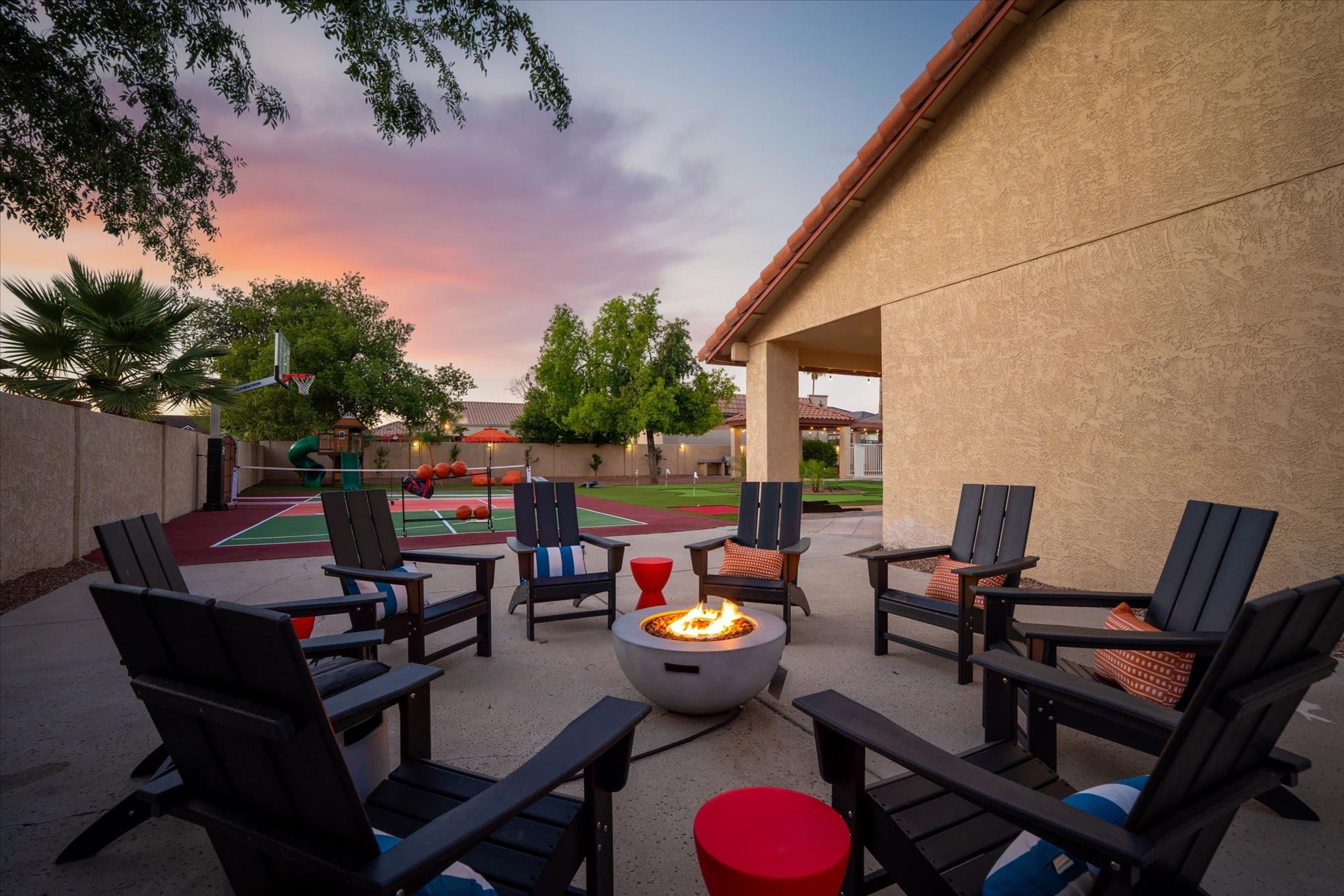 An outdoor seating area with Adirondack chairs, a fire pit, and a basketball court.