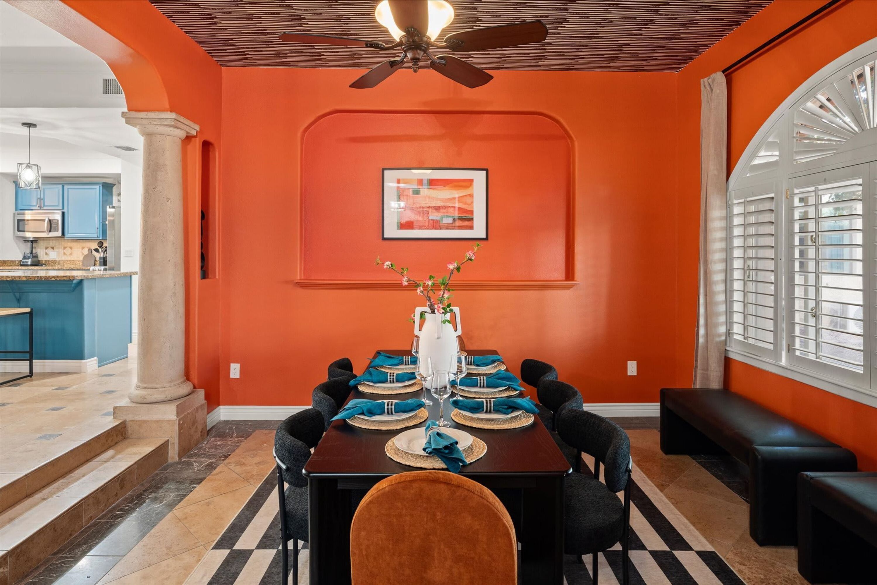 A dining area with a table set for six, a ceiling fan, and a view of the kitchen.
