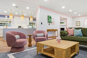 Ein modernes Wohnzimmer mit einer Couch, zwei Sesseln, einem Couchtisch und einer Küche im Hintergrund.