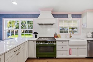 A kitchen with white cabinetry, a green stove, and a view of the backyard through large windows. - Bradenton Beach Club - Poolside Estate Bunkroom (Bradenton)