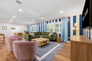 Ein modernes Wohnzimmer mit einem grünen Sofa, rosafarbenen Sessel und einem Couchtisch aus Holz, sowie einem Fernseher auf einem Schrank.