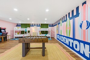 A room with bunk beds, a foosball table, and a wall with a large 'BRADENTON' sign. - Bradenton Beach Club - Poolside Estate Bunkroom (Bradenton)