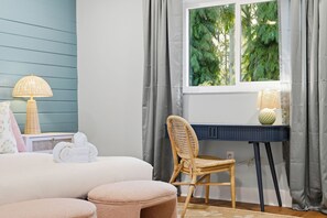 Ein Schlafzimmer mit Bett, Stuhl, Schreibtisch und einem Fenster mit Vorhängen.