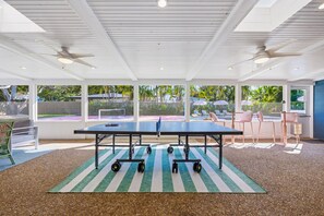 A spacious indoor area with a ping pong table, exercise equipment, and a view of a tennis court. - Bradenton Beach Club - Poolside Estate Bunkroom (Bradenton)