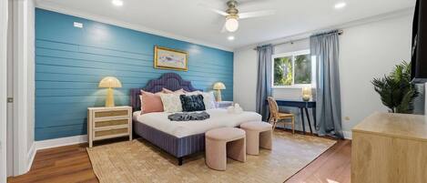 Un dormitorio con cama, mesitas de noche, un escritorio, una silla, televisor y ventana con cortinas.