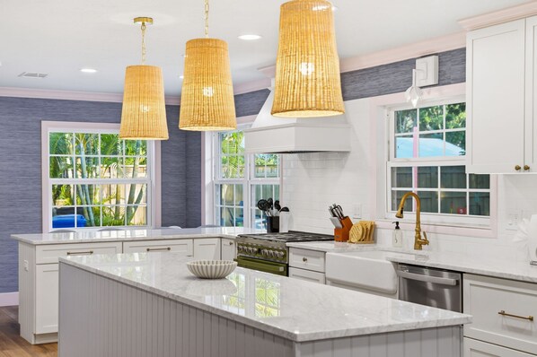 Una cocina moderna con una isla central, iluminación colgante y ventanas amplias.