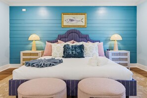 A bedroom with a bed, two bedside tables, lamps, a framed picture, and a blue wall. - Bradenton Beach Club - Poolside Estate Bunkroom (Bradenton)