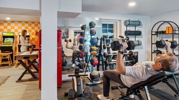 Ein Heimfitnessraum mit Trainingsgeräten, einer Spielkonsole und einer karierten Wand.