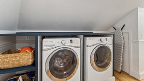 Ein Waschraum mit zwei Waschmaschinen, einem Wäschekorb aus Weidengeflecht und einem weißen Kühlschrank.