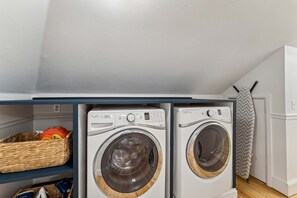 A laundry room with two front-loading washing machines, a wicker basket, and a white refrigerator. - Golf Sim Pickleball Theater Sauna Games Sleeps 24 (Hilton Head Island)