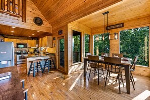 A wooden cabin interior with a kitchen, dining area, and large windows overlooking greenery. - Private Mtn Views Movie Theater Hot Tub Pool Table (Sevierville)