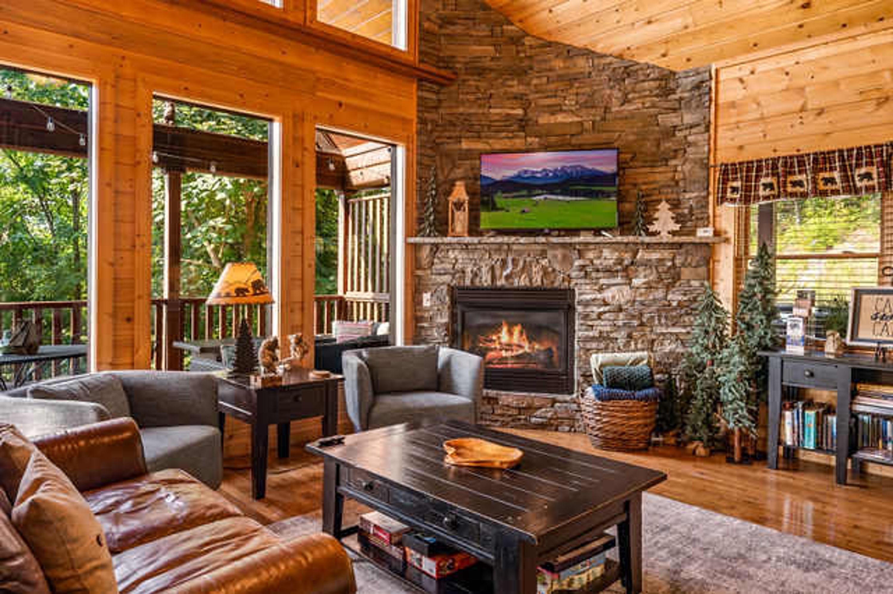 A cozy living room with a stone fireplace, comfortable seating, and a large window overlooking greenery.