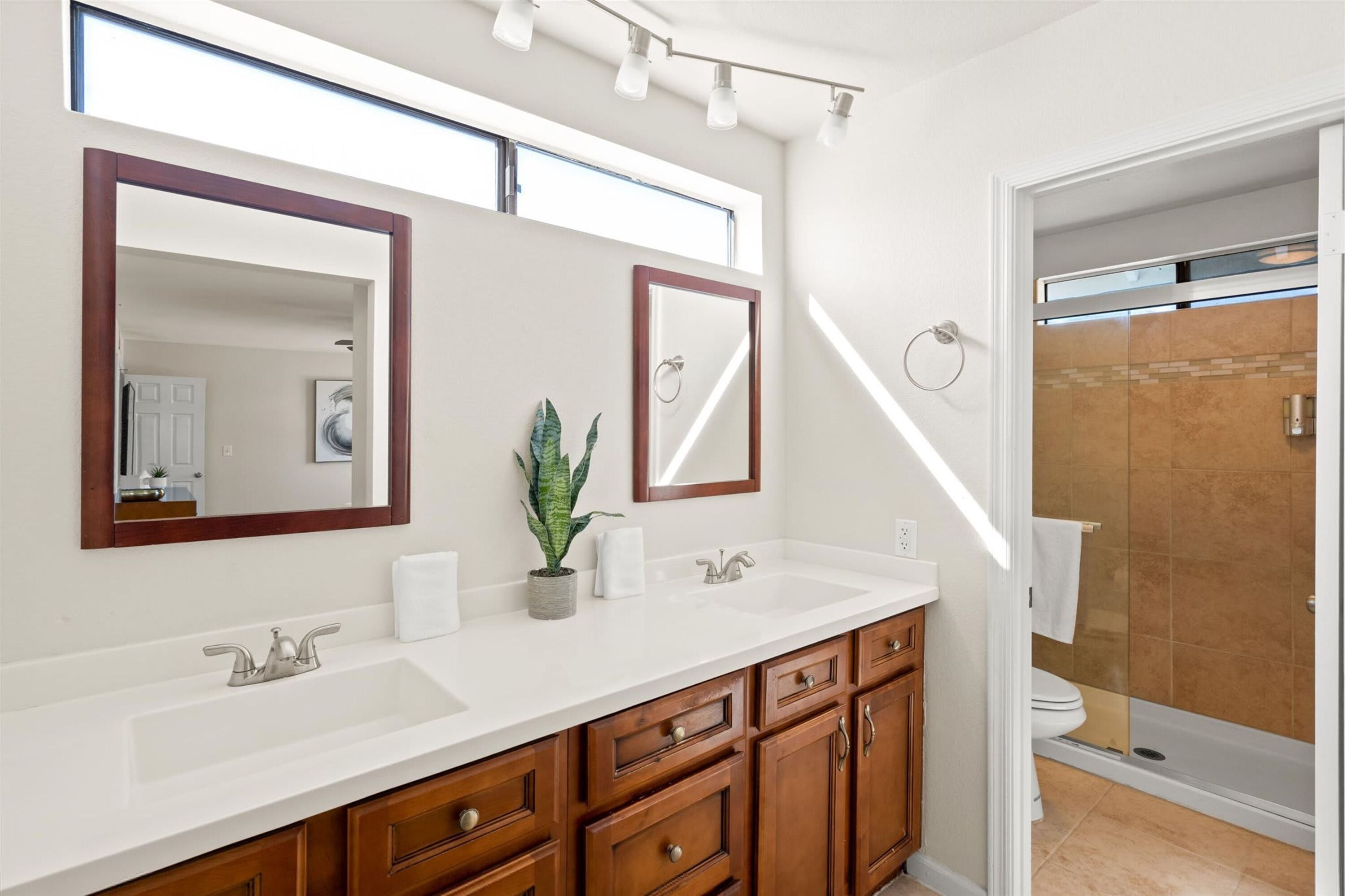 A modern bathroom with a double sink vanity, wooden cabinets, and a shower area.