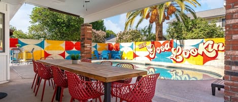 Une terrasse extérieure avec une piscine, des chaises rouges et une fresque murale.