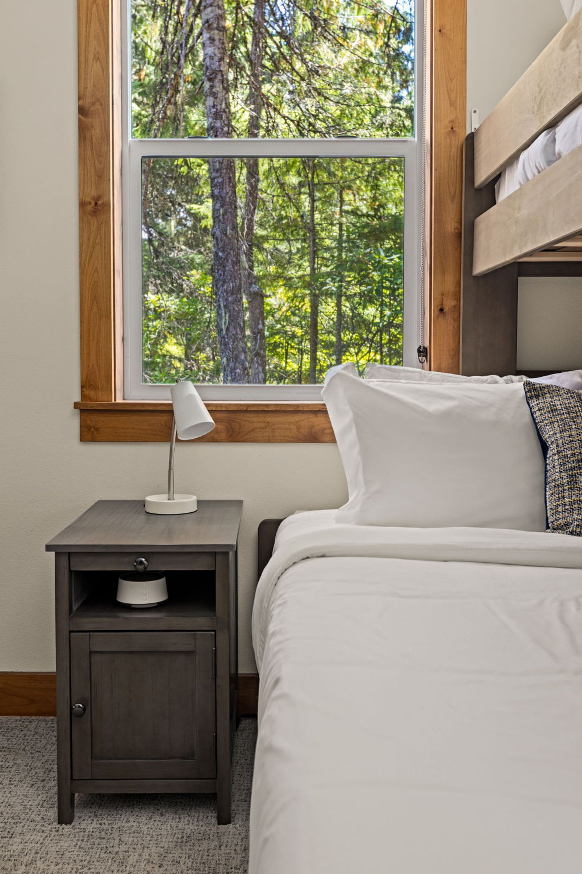 Un dormitorio con ventana, mesita de noche, lámpara, cama y literas.