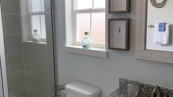 A bathroom with a shower, toilet, sink, and a window with decorative items.