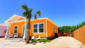 A single-story house with a bright orange exterior, a palm tree, and a fenced yard. - Beach Please- Family Friendly Community Pool (Port Aransas)