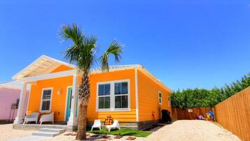 A single-story house with a bright orange exterior, a palm tree, and a fenced yard.