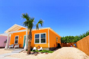Ein einstöckiges Haus mit leuchtend orangefarbener Fassade, einer Palme und einem umzäunten Garten.