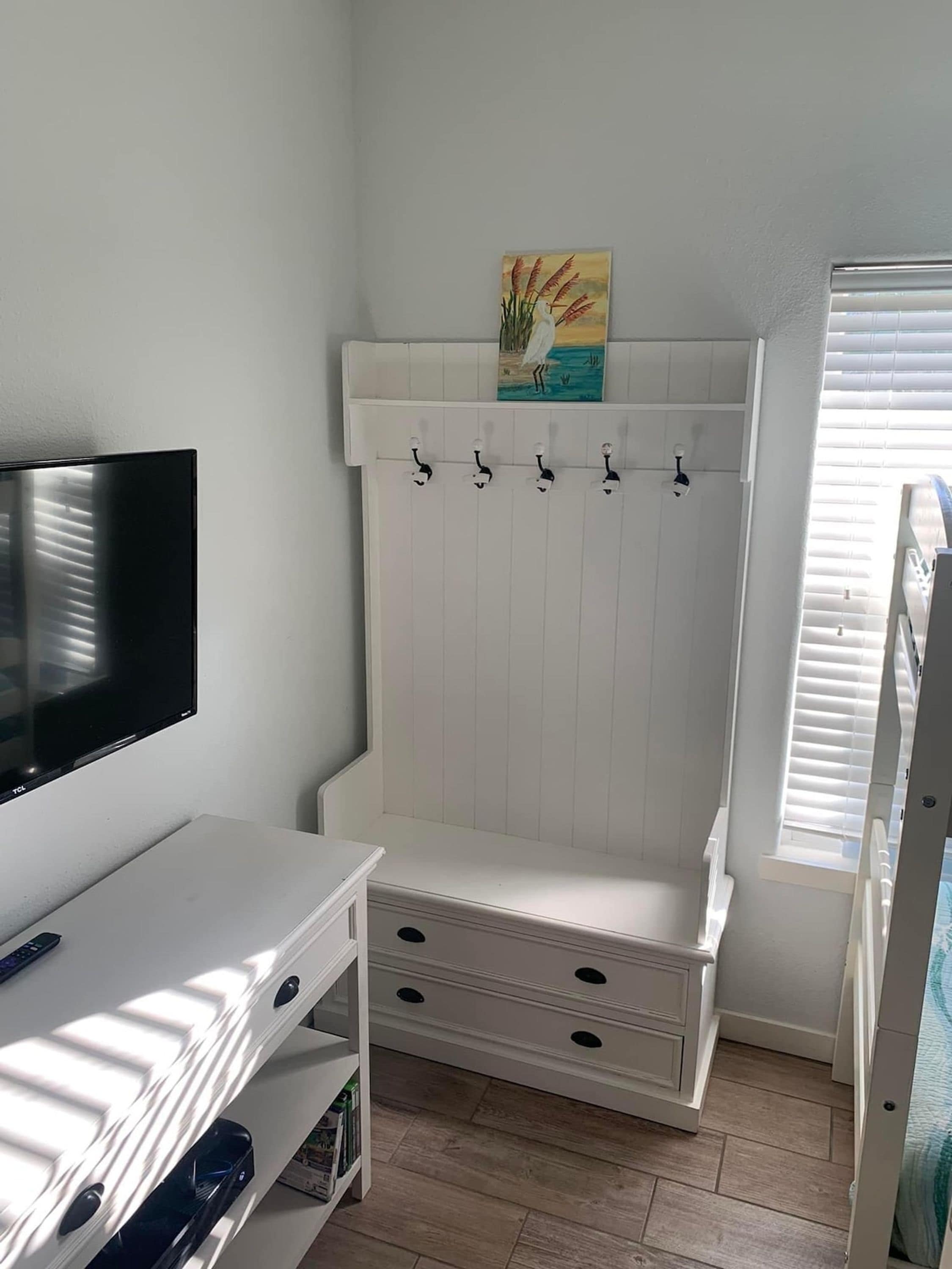 A child's room with a TV, a white cabinet, a coat rack, and a painting on the wall.