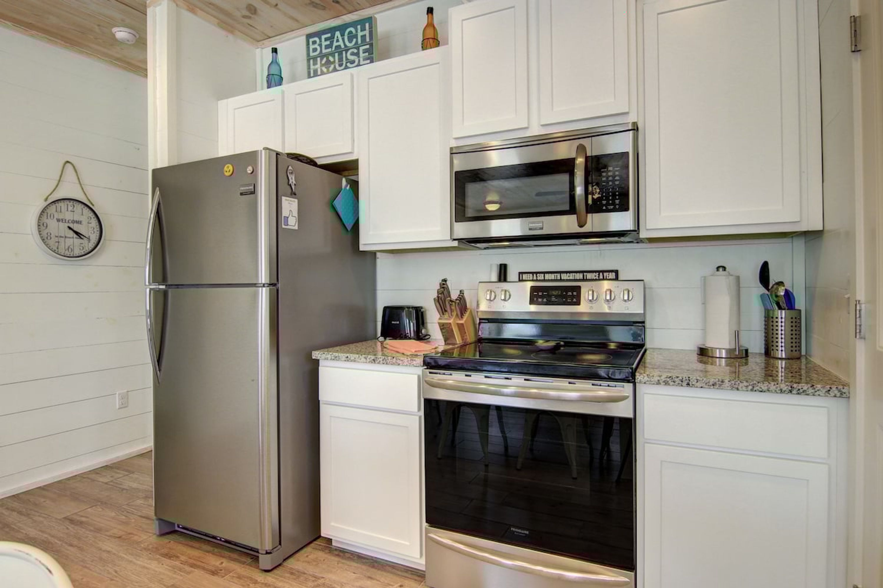 A kitchen with a stainless steel refrigerator, a microwave, an oven, and a clock on the wall.