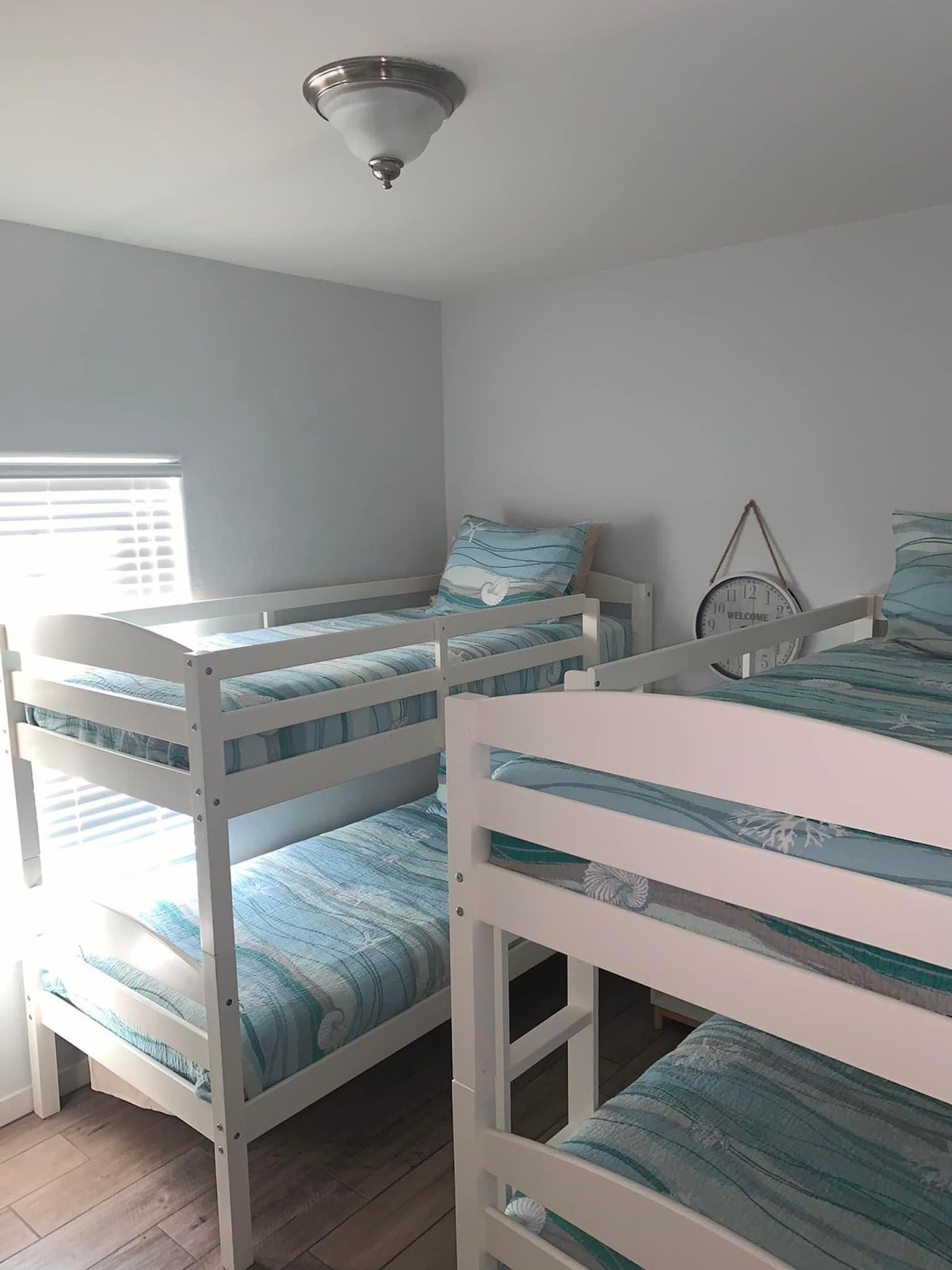 A bunk bed room with a ceiling fan, a clock, and a window with blinds.