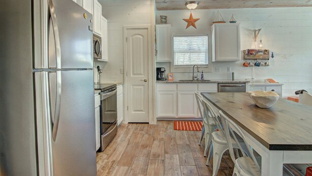 A kitchen with white cabinetry, a stainless steel refrigerator, a wooden island with stools, and a star decoration on the ceiling. - Beach Please- Family Friendly Community Pool (Port Aransas)