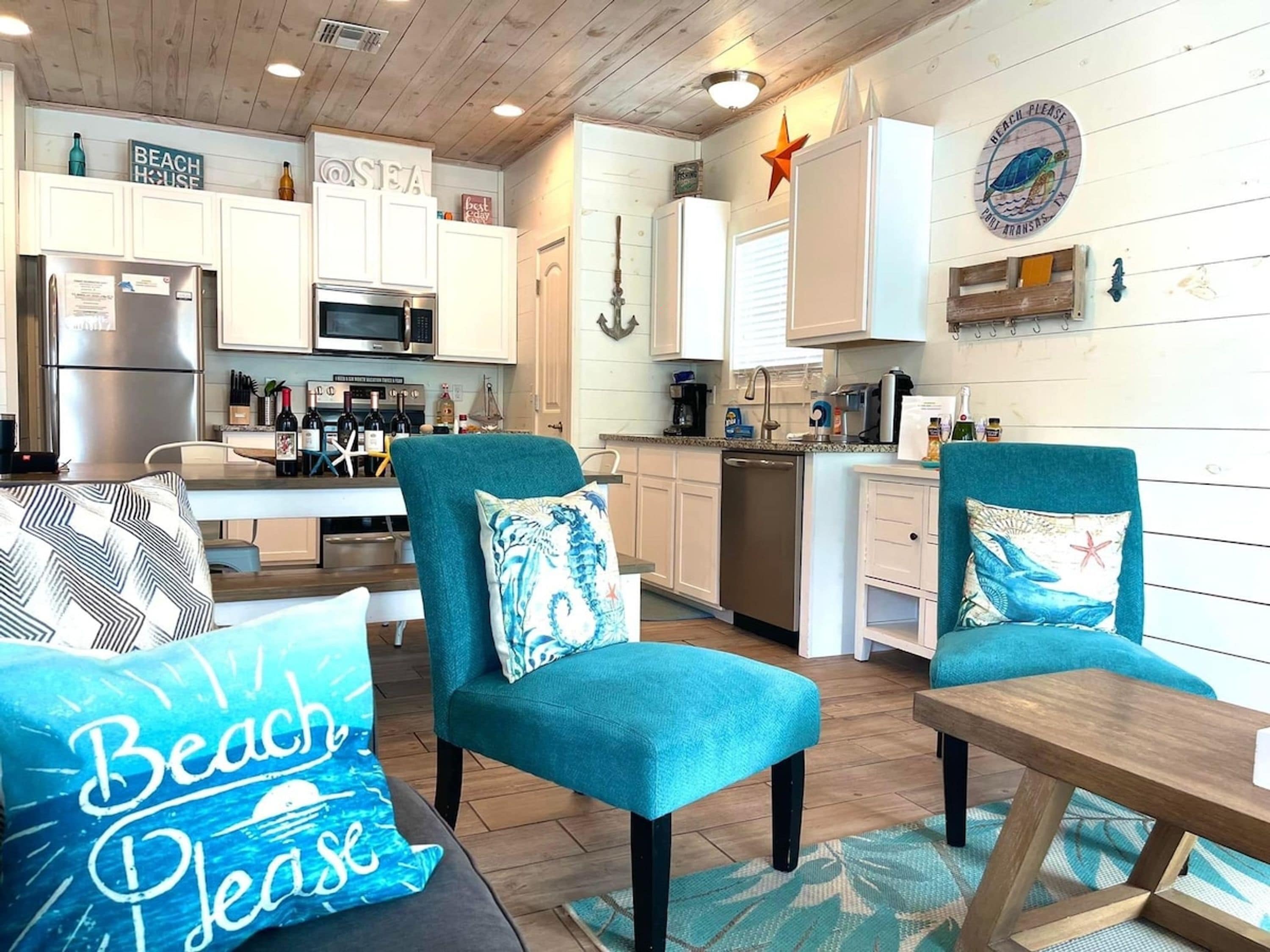 A kitchen with white cabinets, a microwave, and a refrigerator. There are two teal armchairs with decorative pillows.