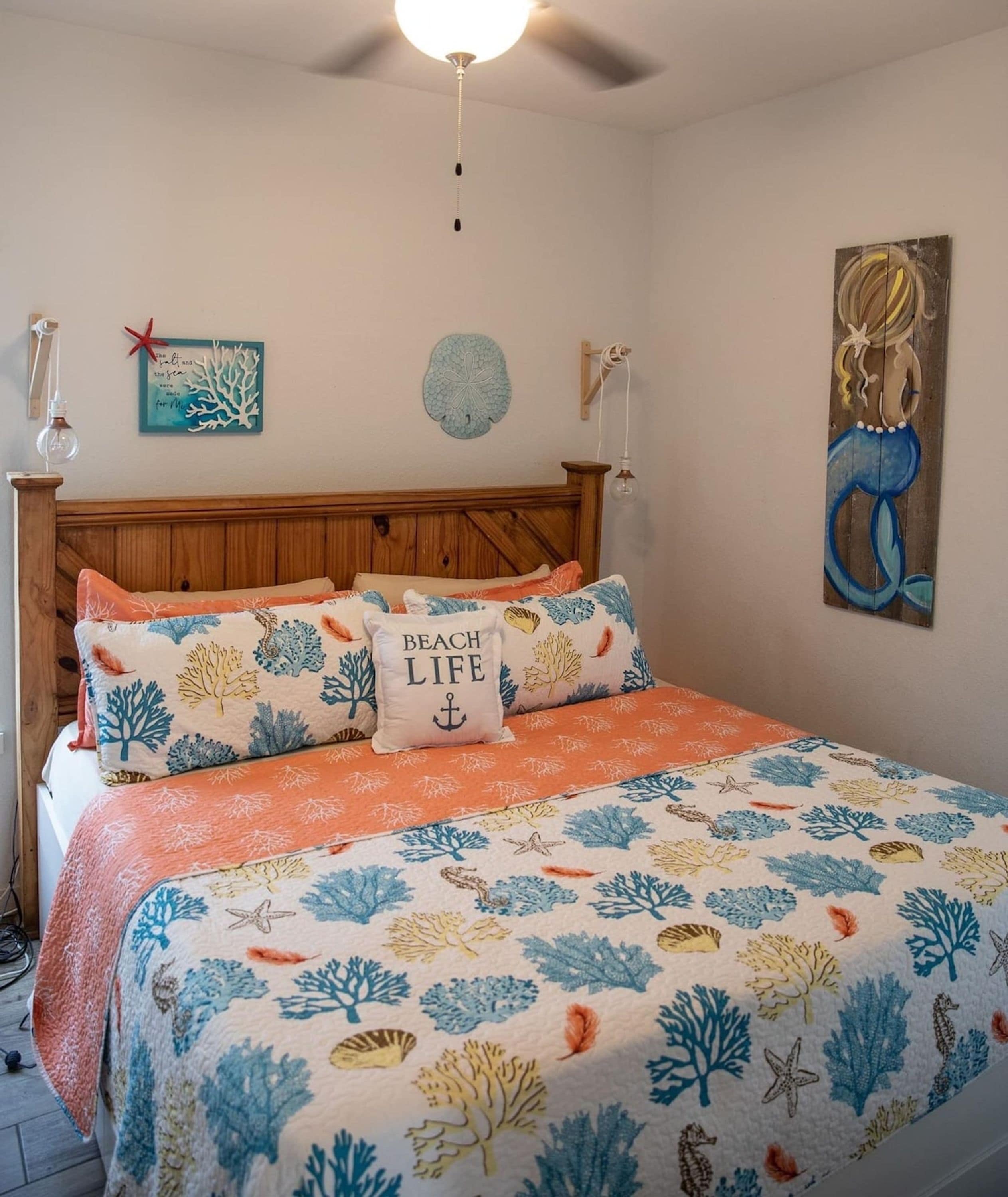 A bedroom with a bed featuring a beach-themed bedspread, a wooden headboard, and a wall with nautical decor.