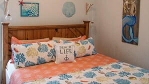 A bedroom with a bed featuring a beach-themed bedspread, a wooden headboard, and a wall with nautical decor. - Beach Please- Family Friendly Community Pool (Port Aransas)