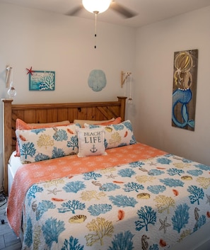 Ein Schlafzimmer mit einem Bett, das mit einem Bettbezug mit Strandmotiv, einem Holz-Kopfteil und einer Wand mit maritimer Dekoration ausgestattet ist.